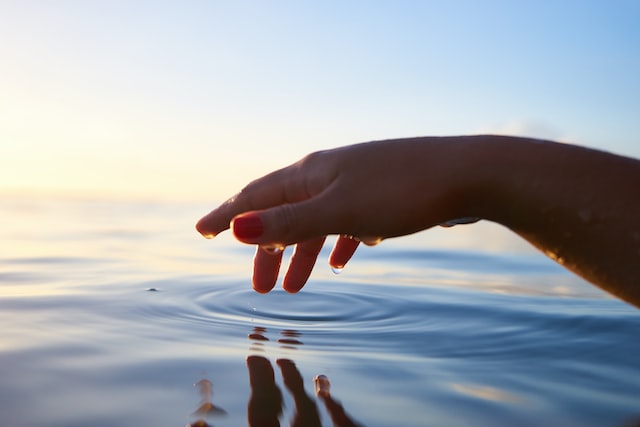 Weltwassertag: Hand berührt Meer mit Sonnenaufgang im Hintergrund